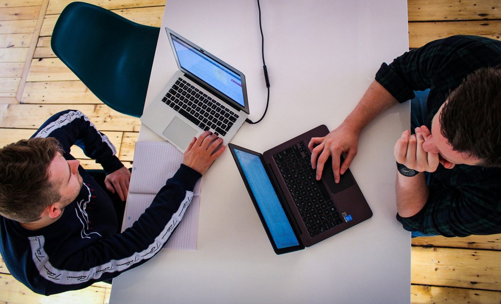 two men sitting at a table working on laptops